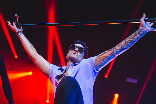 man with tatoos and sunglasses hold mic stand overhead on stage